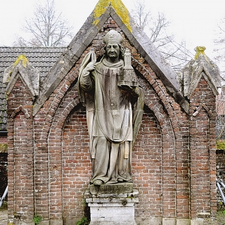 214-Het Sint-Willibrordusbeeld staat op het kerkhof, achter de Willibrorduskerk te Bakel. Het is een zandstenen beeld en komt uit 1862.