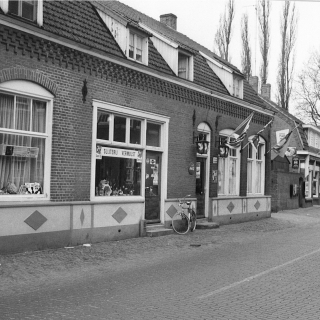 316-Nu ’t Viltje in Bakel, maar vroeger waren hier de volgende winkels/zaken gevestigd. Van links naar rechts: kapper Tjeu Vermulst, slijterij Ad Vermulst en café De Zwaan. In het volgende gebouw is tegenwoordig de apotheek gevestigd. Op de achtergrond zie je café De Kroon (nu Jut en Jul). Foto gemaakt rond 1960.