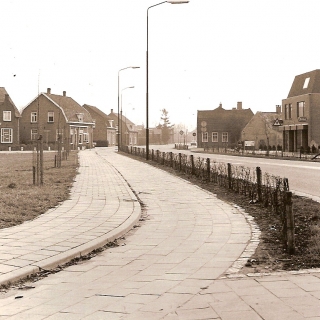 319-Foto genomen tussen 1980 en 1990 vanaf de rotonde in het centrum. Met winkels aan de Schoolstraat en de van de Poelstraat in Bakel.